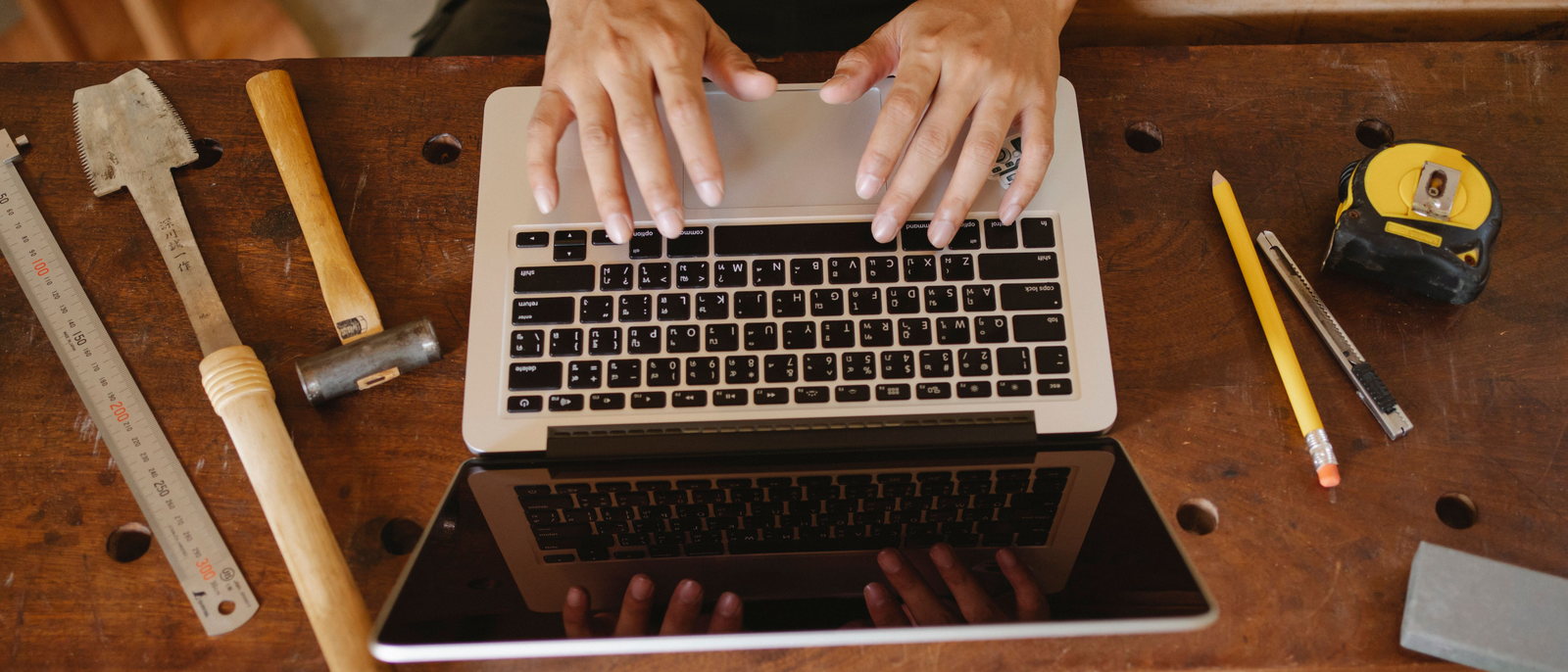 Selbstständige Handwerkerin sitzt in ihrer Werkstatt am Laptop und sortiert Belege